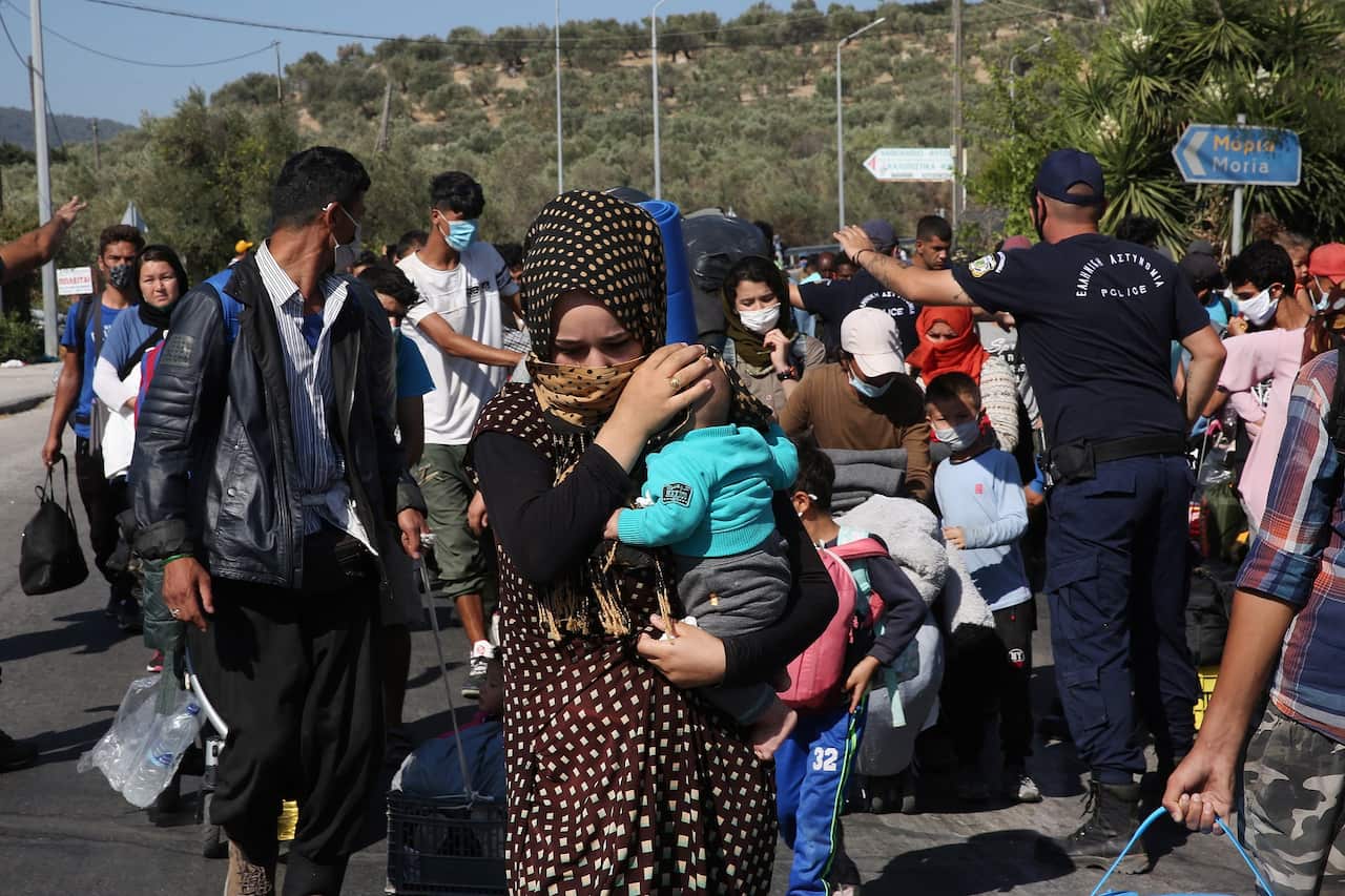 Asylum seekers carry their belongings as they walk on a roadside, near the destroyed Moria refugees camp.
