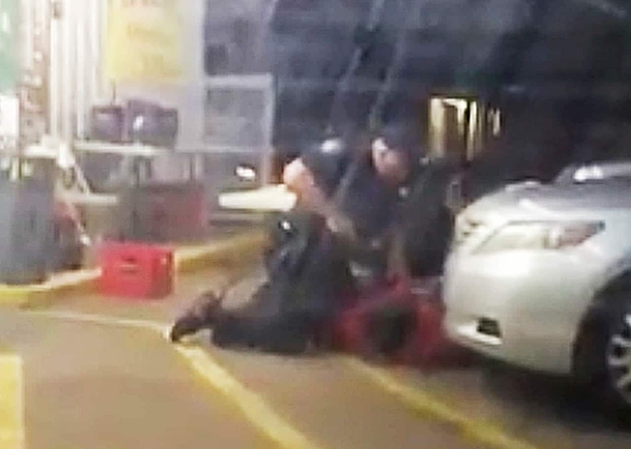 Alton Sterling is restrained by two Baton Rouge police officers, one holding a gun, outside a convenience store.