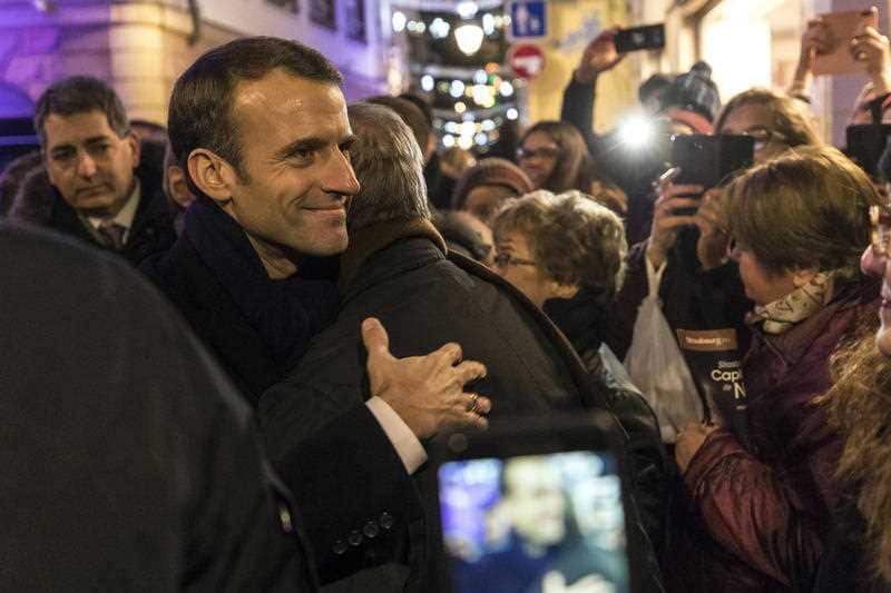 French President Emmanuel Macron (2-L) hugs a visitor to the Christmas market, as he visits the terror attack scene, in Strasbourg.