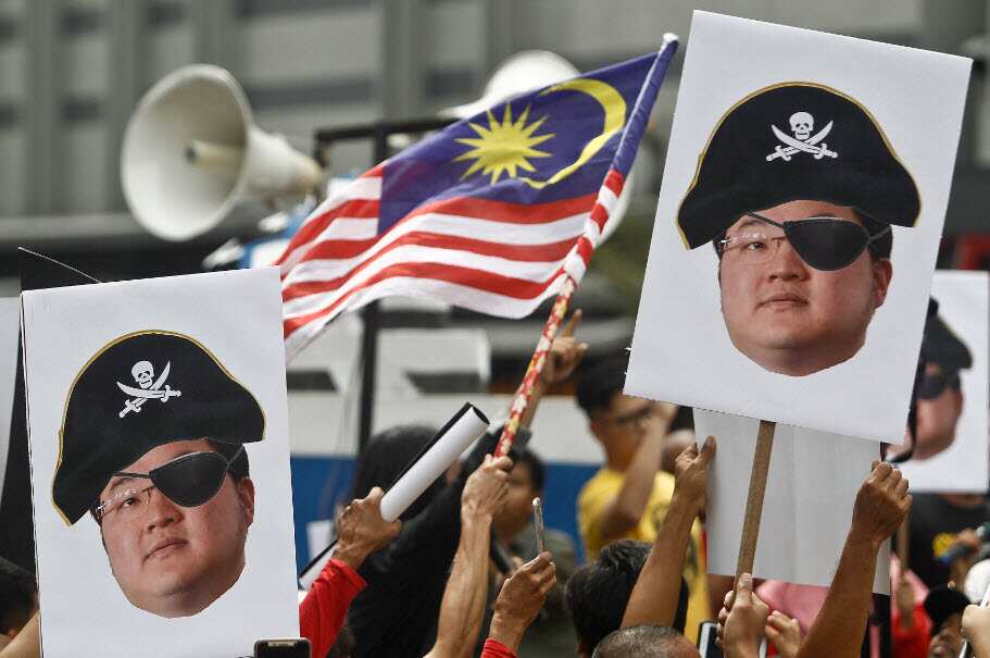 FILE - Protesters hold portraits of Malaysian financier Jho Low illustrated as a pirate during a protest in Kuala Lumpur 