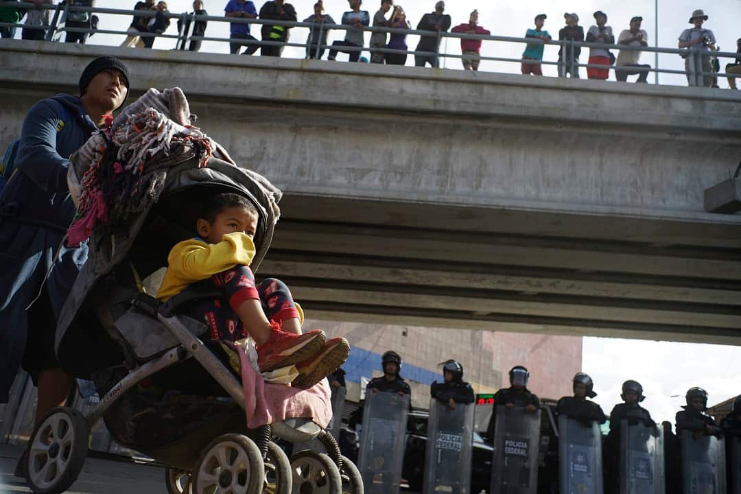 A migrant man pushes a child in a stroller past a cordon of riot police as he joins a small group of migrants trying to cross the border.