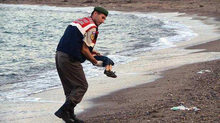 A paramilitary police officer carries the lifeless body of a migrant child after a number of migrants died