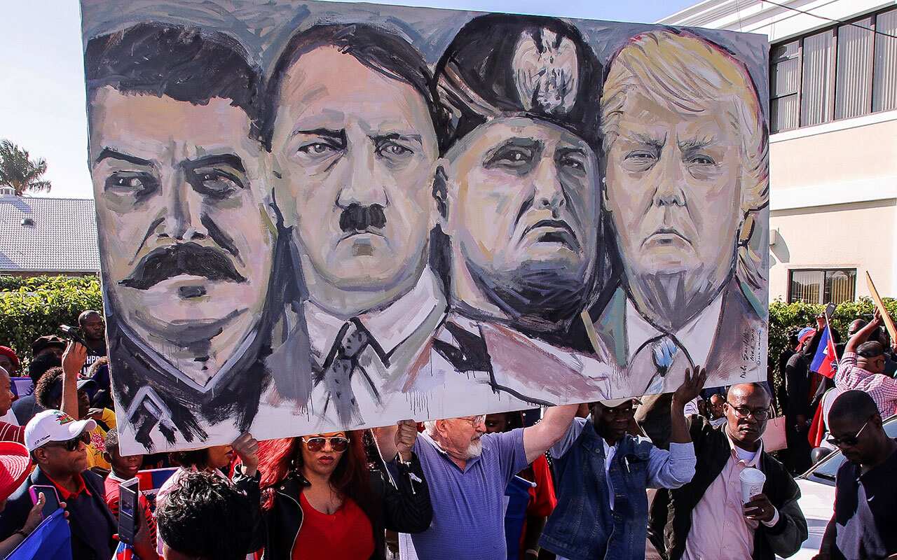 Haitian community members hold an image depicting image shows from left, Joseph Stalin, Adolf Hitler, Benito Mussolini and President Donald Trump.