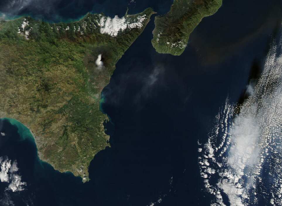 The ash plume from the eruption is seen to the east over the ocean
