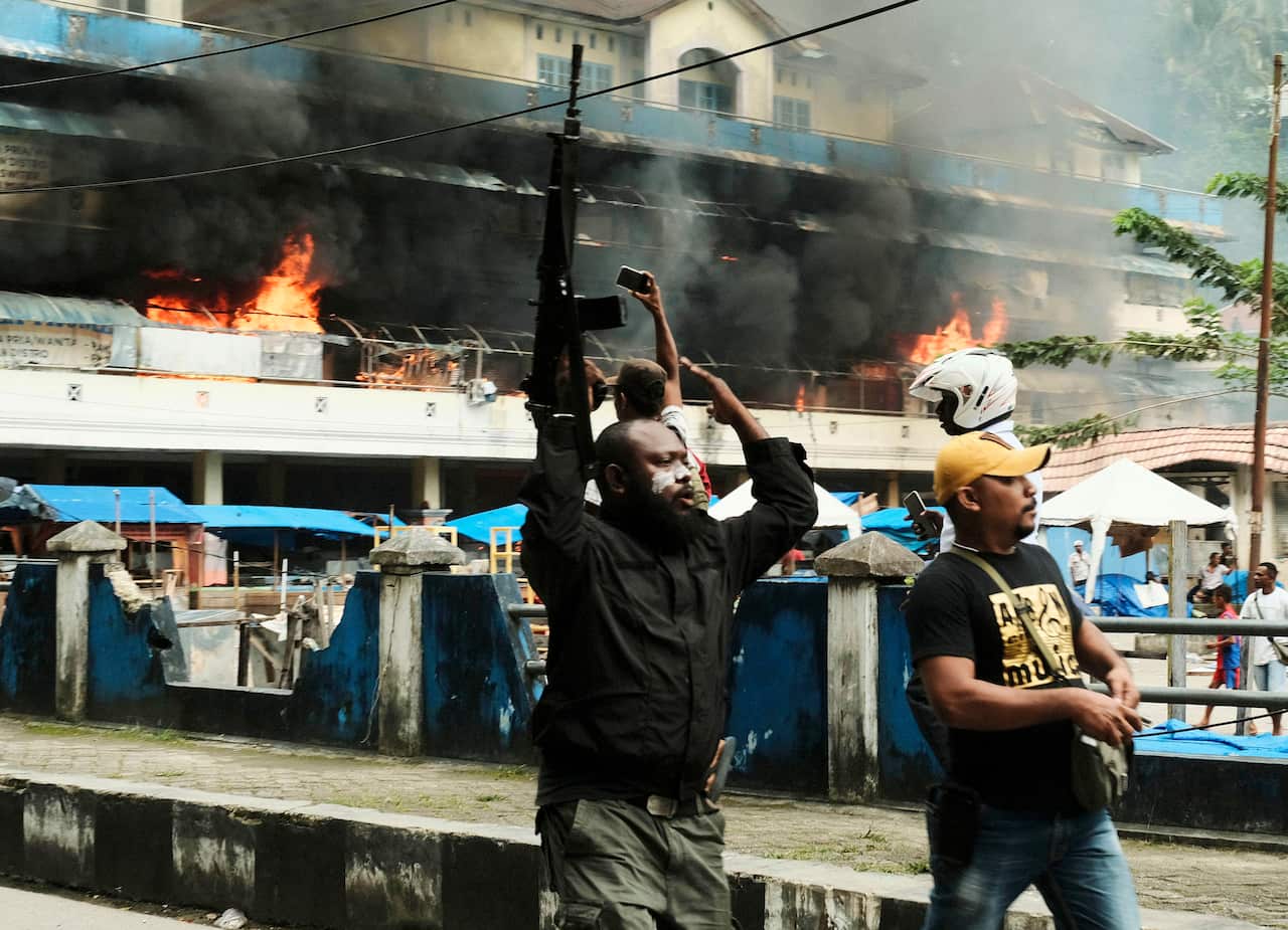 A police officer raises his rifle as the market burns during the protests.