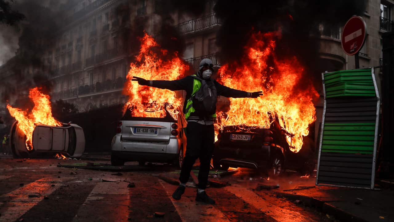 Protesters wearing yellow vests (gilets jaunes) set cars and barricade on fire as they clash with riot police.