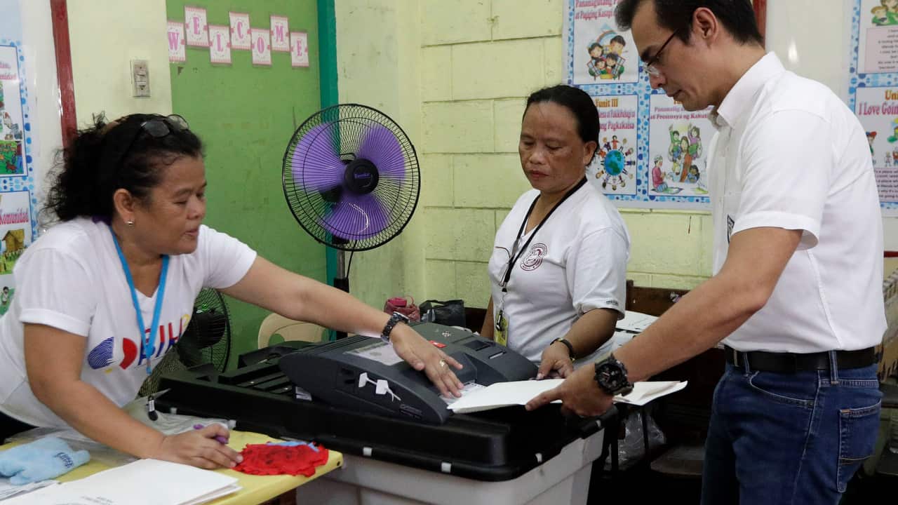 Manila mayor candidate Francisco "Isko" Moreno Domagoso, right, is helped by election workers as he casts his vote in Manila.