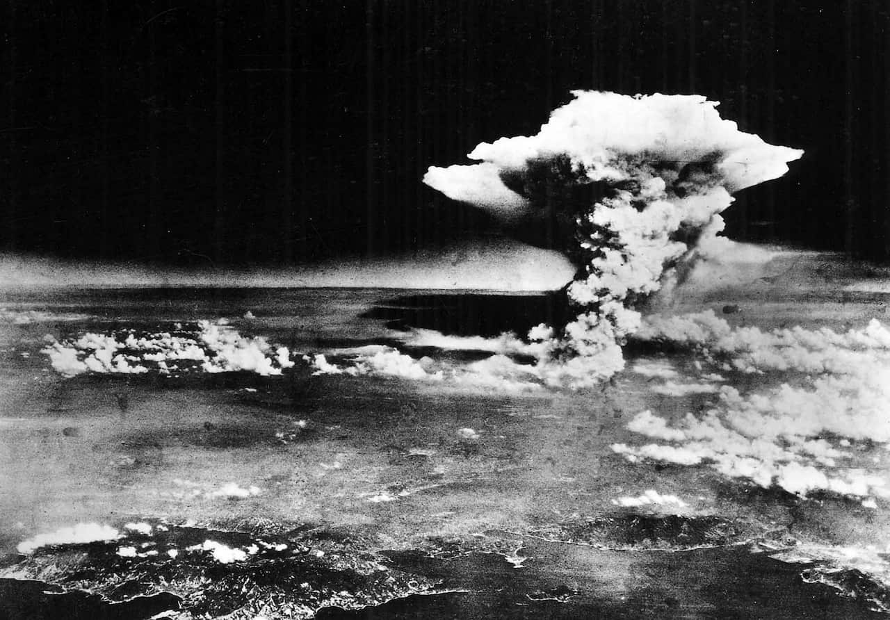 A greyscale image of thick plumes of smoke rising from the ground against a black sky.