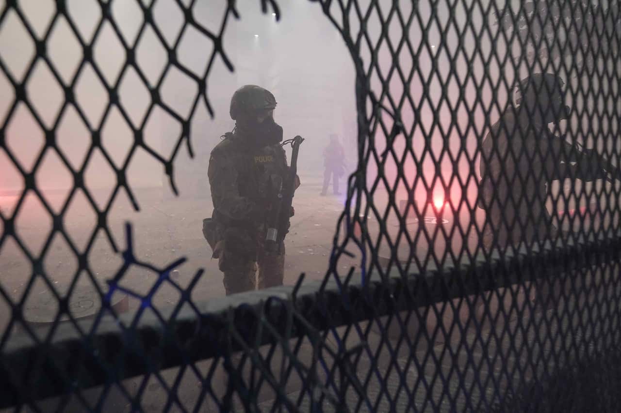 A federal officer stands guard behind a hole in the fence blocking access to the federal courthouse in Portland on 24 July 2020.