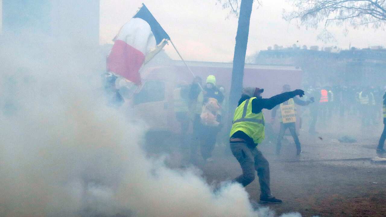 A yellow vest protester throws debris at riot police amid tear gas smoke during clashes around the Arc of Triomphe, in Paris.