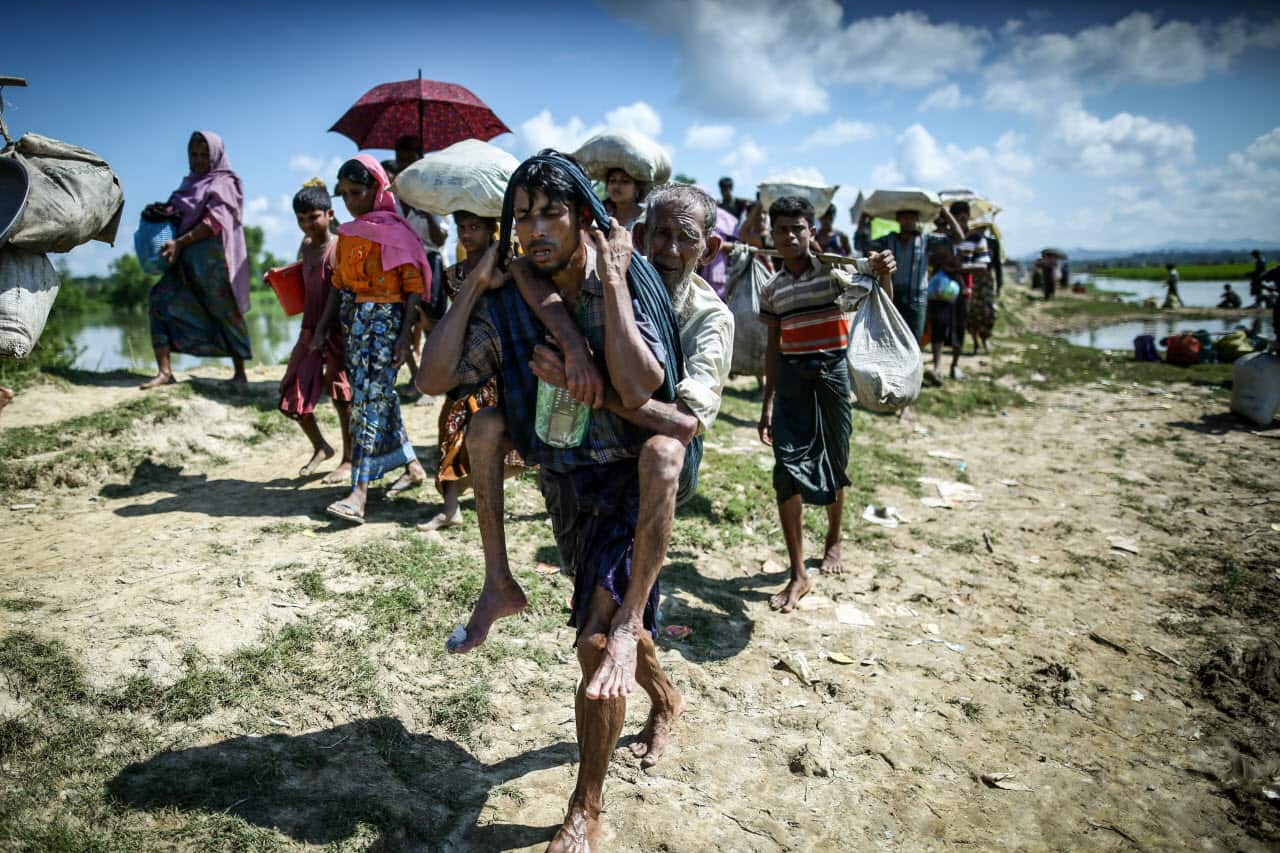 A Rohingya refugee who carries his father for the last 3 days is returned to the quarantine area after waiting hours at the Myanmar-Bangladesh border.