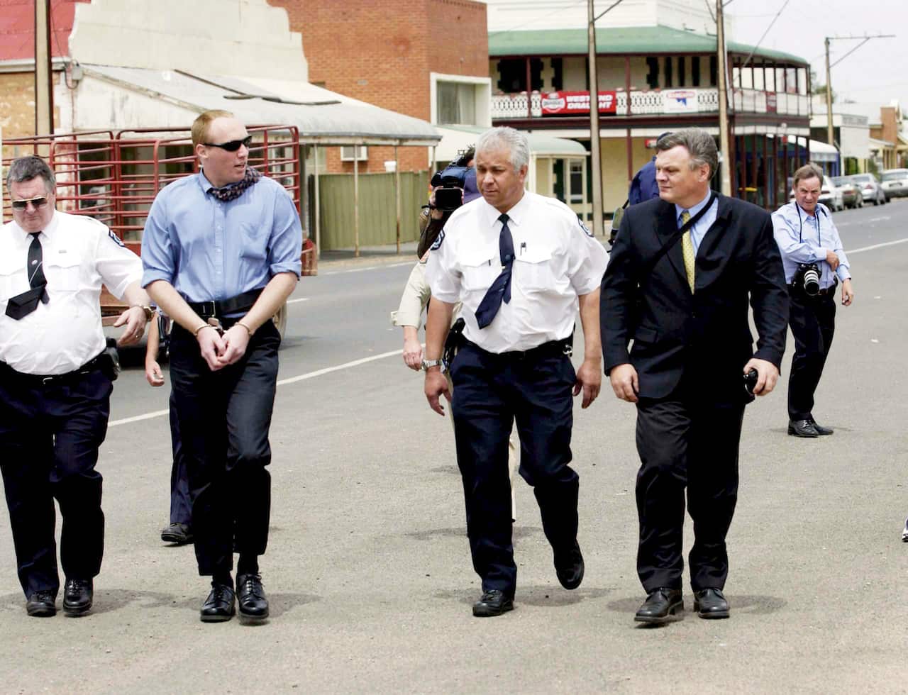 Wagner is escorted handcuffed by court officers outside the disused bank vault (pictured in background) in Snowtown.