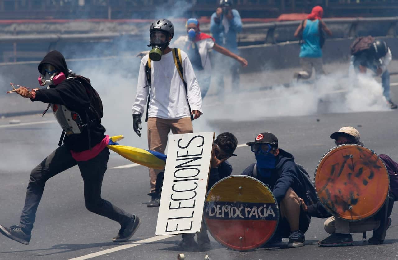 Opponents of President Nicolas Maduro take cover behind homemade shields during clashes with security forces blocking them (AAP)