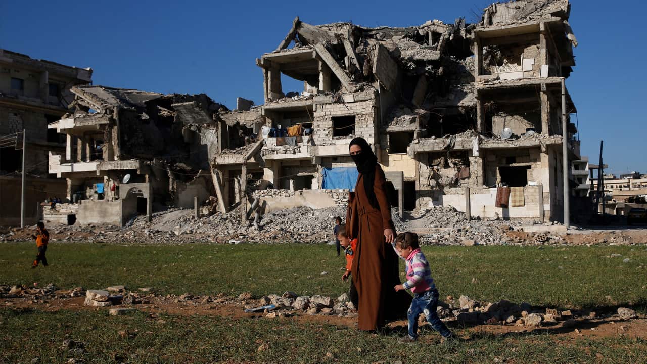 A Syrian woman with her kids walks in front of buildings that were destroyed during the battle between the SDF and IS militants, in Manbi