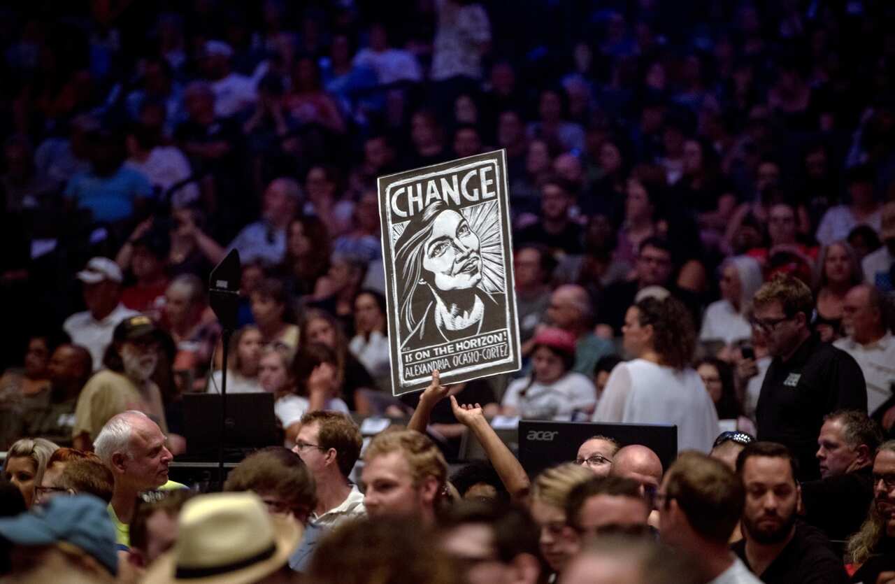 A supporter holds a sign depicting Alexandria Ocasio-Cortez as she speaks at a campaign event for James Thompson.
