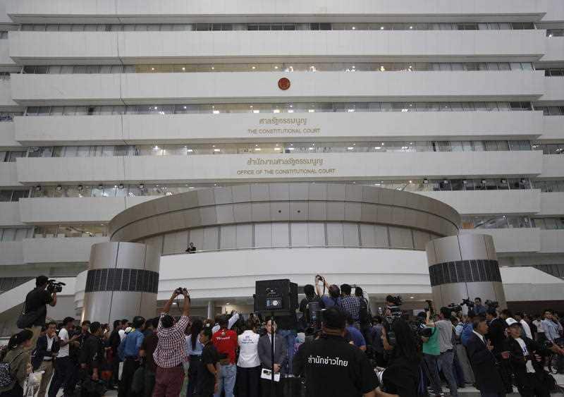 Members of the media and passerby listen as a Thai Constitution Court judge reads the verdict on Thai Raksa Chart Party's dissolution.