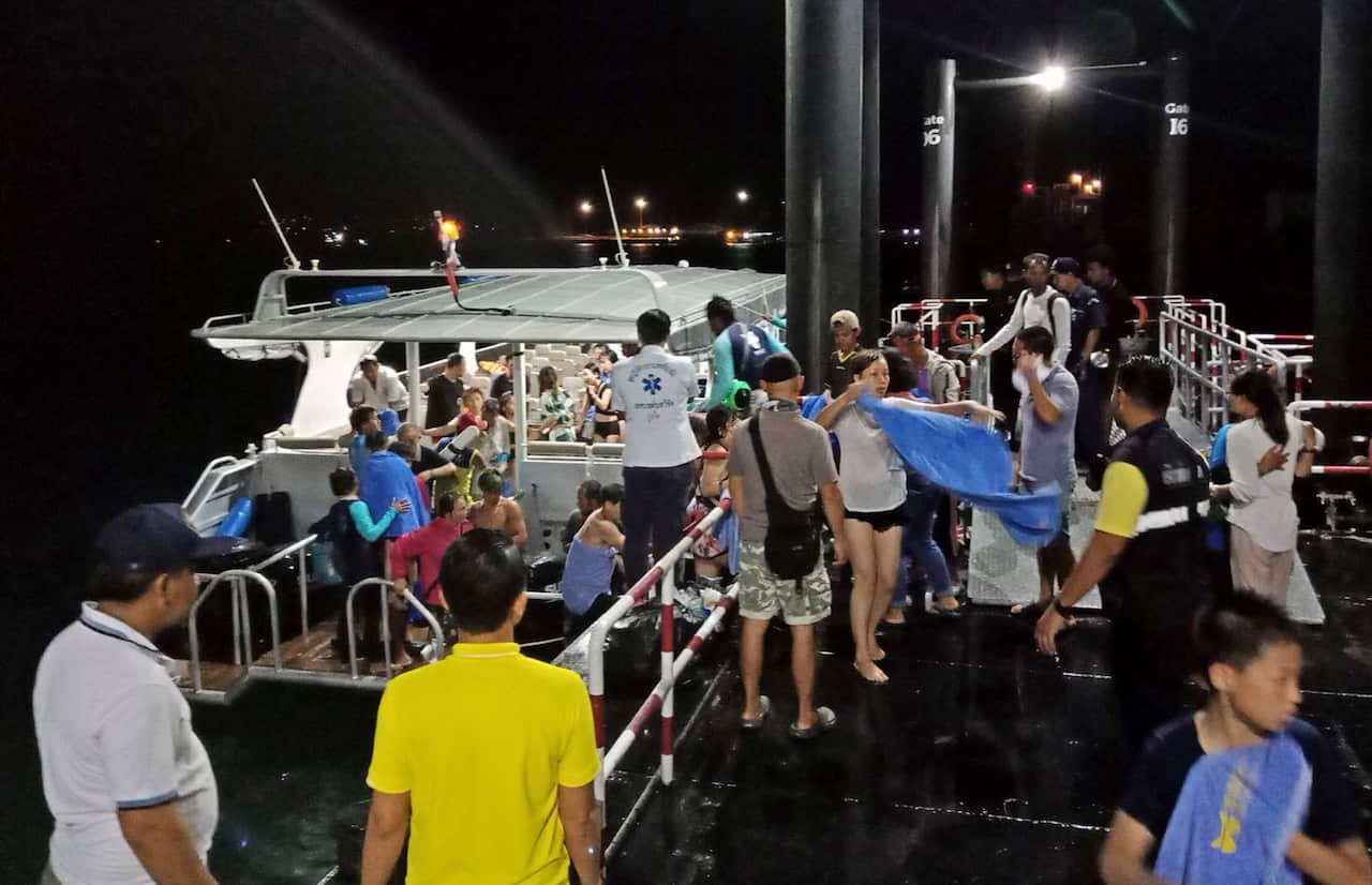 Rescued tourists from a boat that sank are helped onto a pier