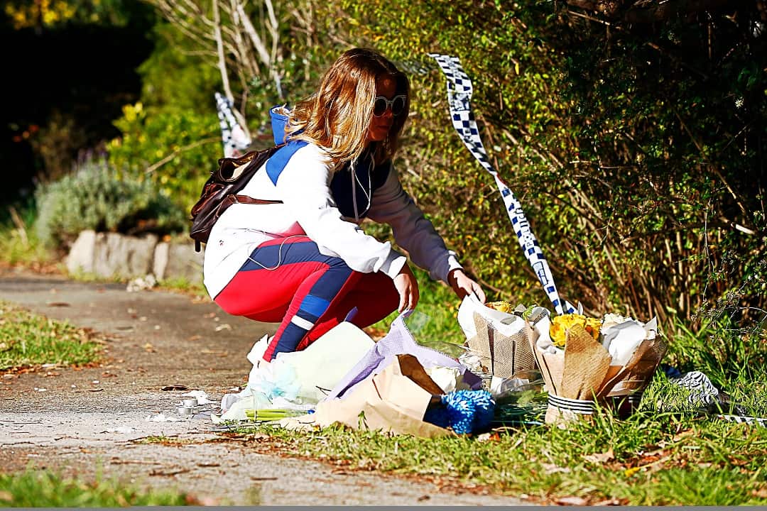 A woman is seen placing flowers at the site of a makeshift memorial at a property in West Pennant Hills, Sydney,