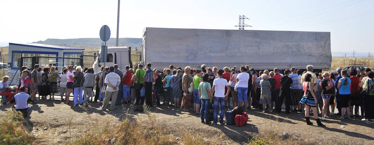 People stand in front of a Russian lorry as it waits at a checkpoint.