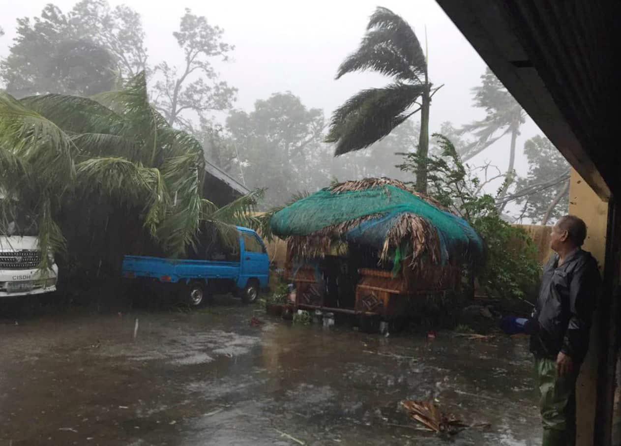 A man takes cover as strong winds and rain topple trees while Typhoon Haima lashes Narvacan, Ilocos Sur, northern Philippines on Thursday Oct. 20, 2016.
