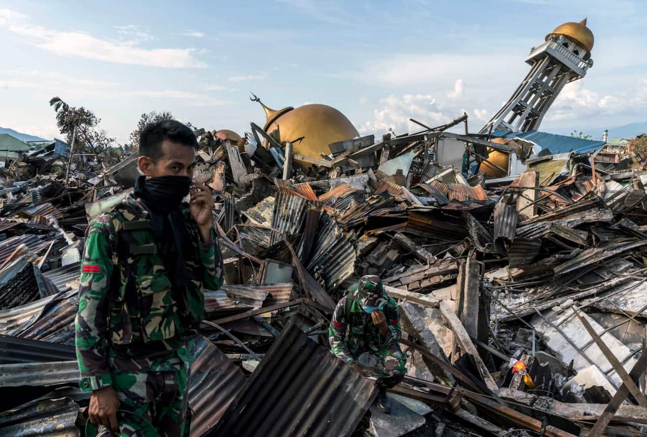 Soldiers on Wednesday, Oct. 3, 2018, look on as rescue workers attempt to recover the body of a child killed in last Friday's earthquake and tsunami 