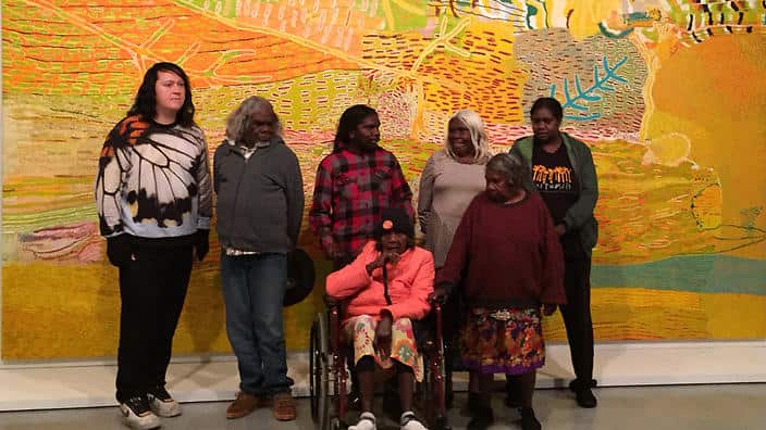Musician Antony Hegarty joins Martu artists in Parnngurr in the east Pilbara region of Western Australia stand with their work 'Kalyu'. Hegarty has been raising awareness of the Martu fight against mining on their land (SBS)