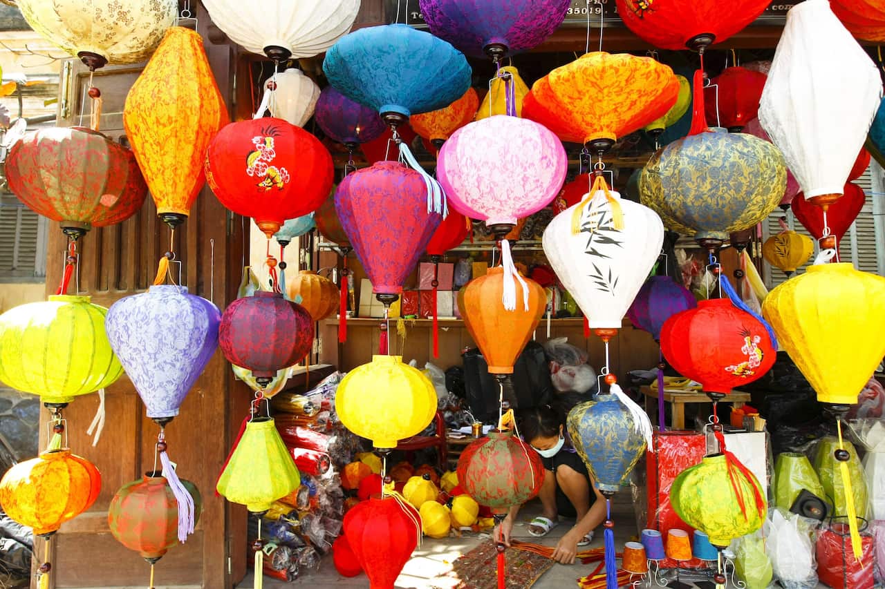 A woman making a lantern as they are displayed in front of a shop in Hoi An