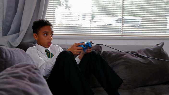 Schoolboy sitting on sofa playing with games console