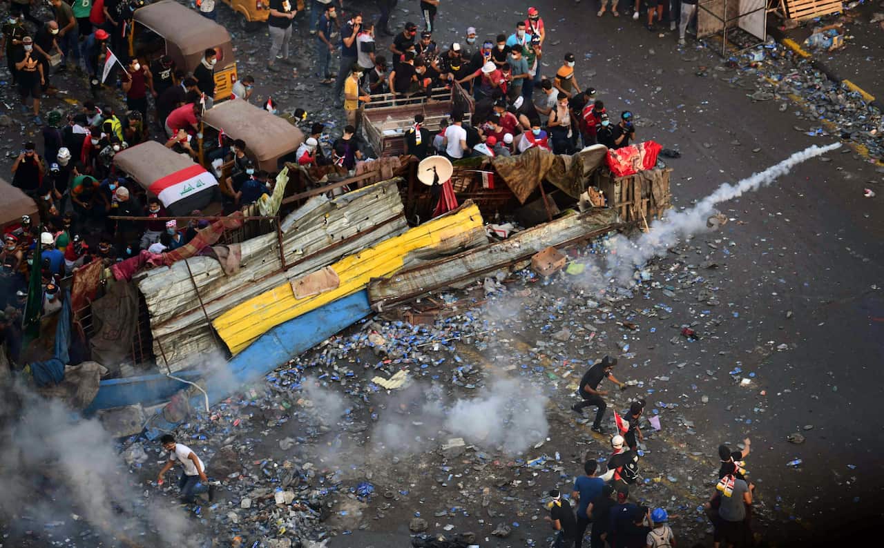 Iraqi protesters throw tear gas canisters back toward riot police forces during a protest in central Baghdad.