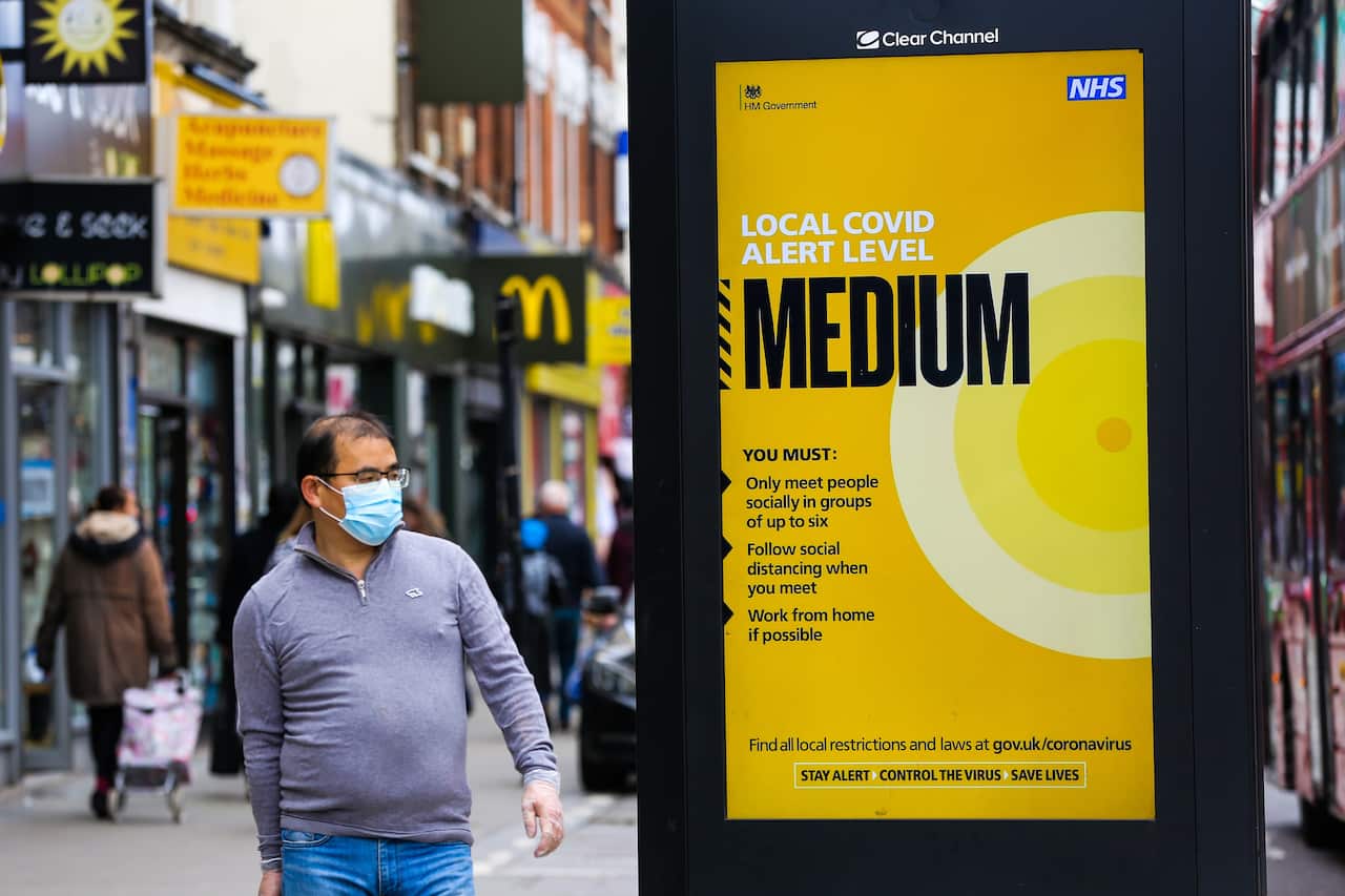 A man wearing a face mask walks past a public information poster in London, as the capital moves to tier two restrictions.