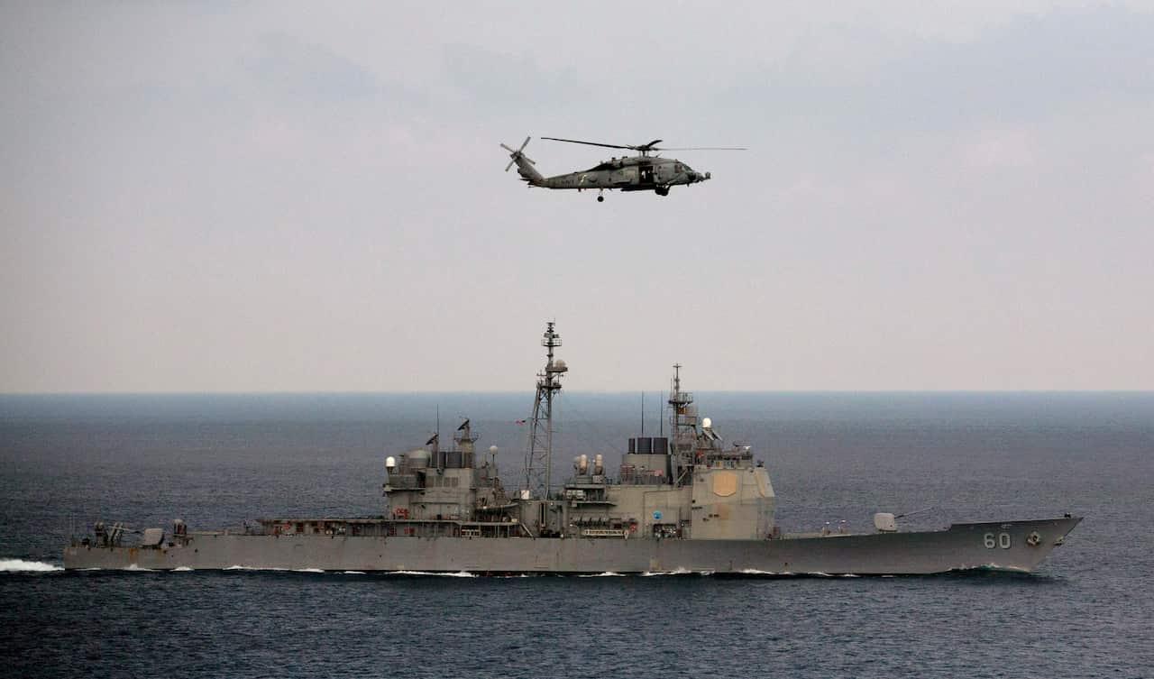 A U.S. Navy helicopter approaches to land on the deck of aircraft carrier USS Theodore Roosevelt (CVN 71), a missile cruiser and a nuclear-powered submarine, as the USS Normady sails in the Bay of Bengal during Exercise Malabar 2015, some 152 miles off ea