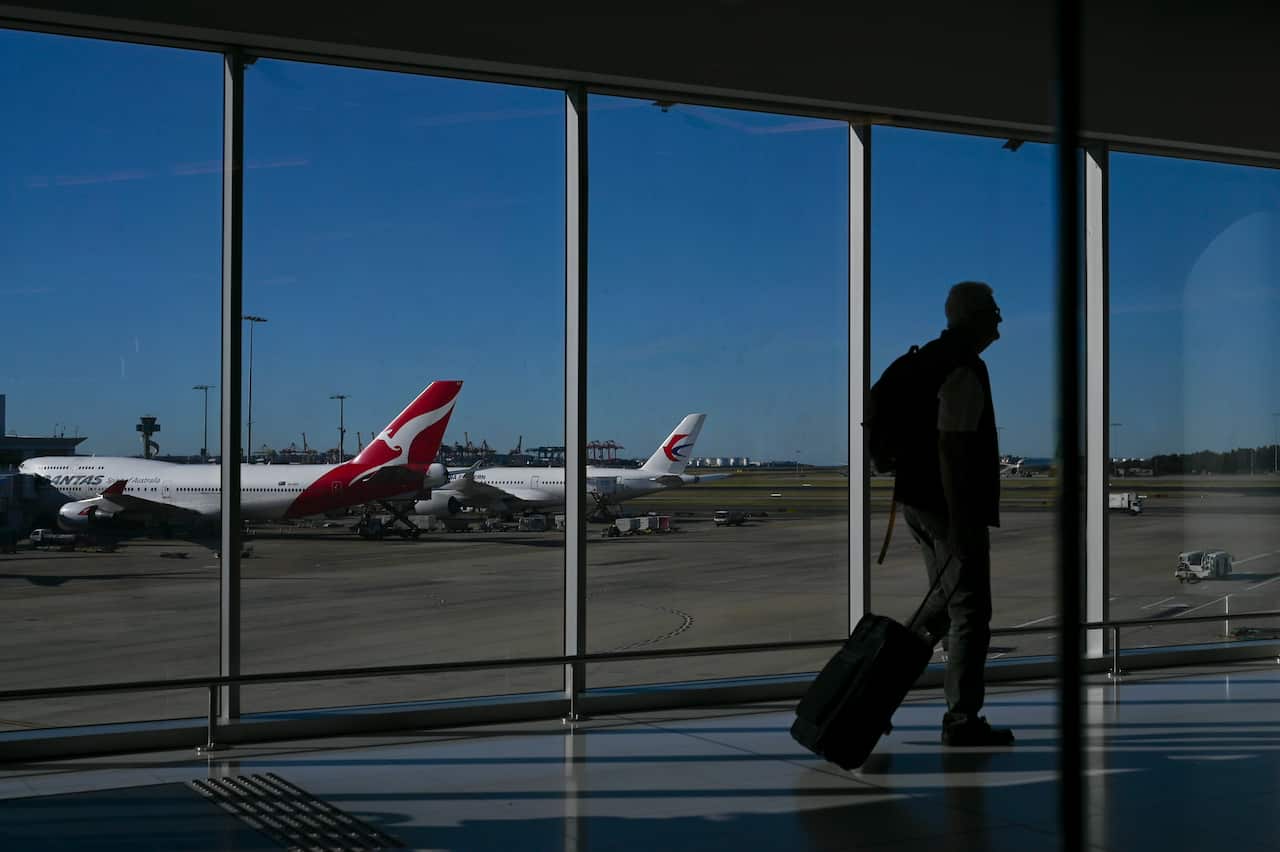 A Qantas plane is seen as a passengers walks to catch a flight at Sydney International Airport in Sydney, Wednesday, August 21, 2019. (AAP Image/Lukas Coch) NO ARCHIVING
