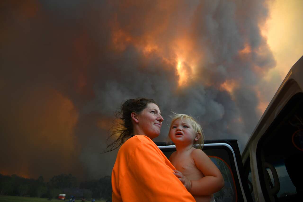 Sharnie Moran and her 18 months old daughter Charlotte look on as thick smoke rises from bushfires near Nana Glen, near Coffs Harbour,