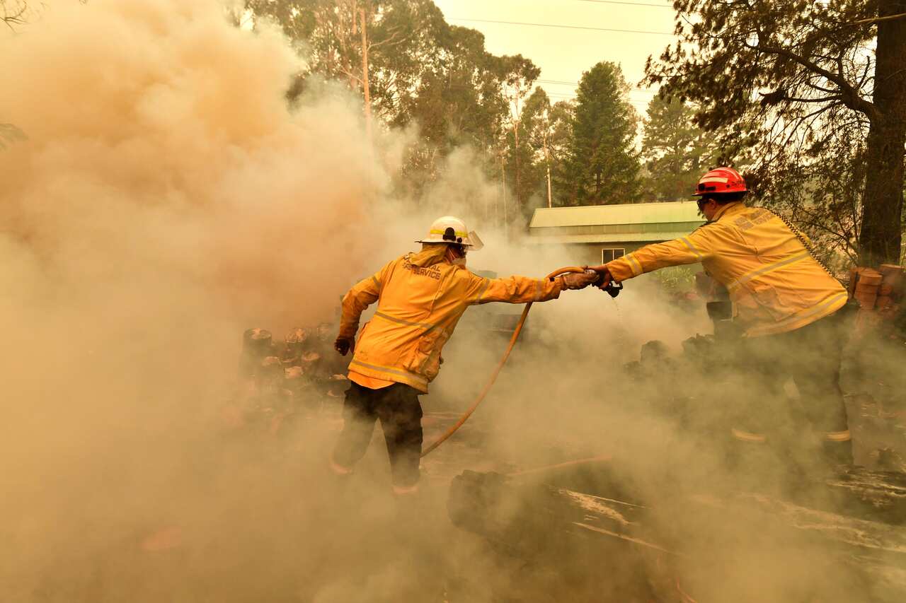 Firefighters hose down a burning woodpile during a bushfire in Werombi, 50km south west of Sydney, Friday, December 6, 2019. 