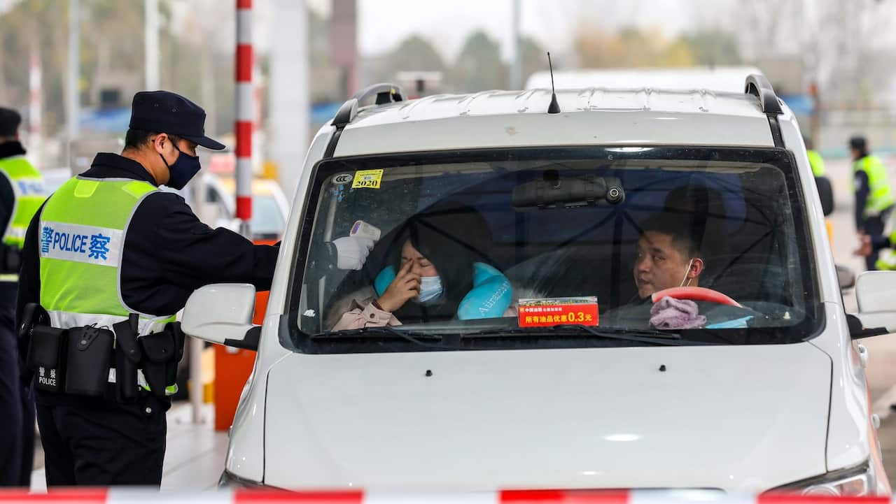 Un miembro del ejército verifica la temperatura corporal de un pasajero en un vehículo en una autopista de peaje en Wuhan, provincia de Hubei, en el centro de China, el 23 de enero de 2020. 