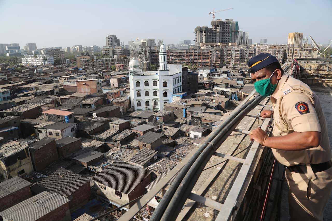 an Indian police officer keeps watch from atop a building over Dharavi, one of Asia's largest slums, during lockdown to prevent the spread of the new coronavirus in Mumbai, India.
