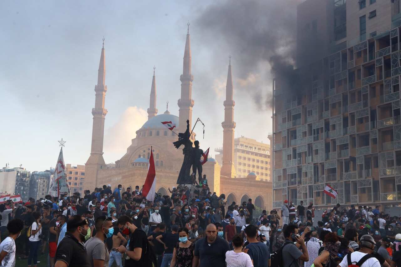 Smoke rises from the Beirut Gardens building as Lebanese people gather at Martyr's Square.
