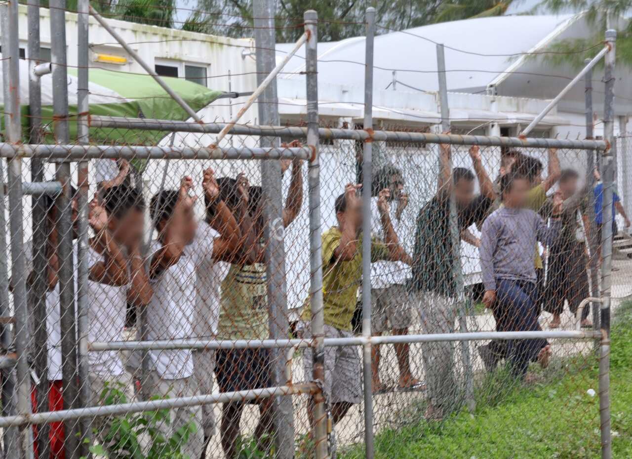 Asylum seekers stand behind a fence in Oscar compound at the Manus Island detention centre in Papua New Guinea.