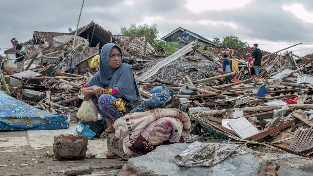 A tsunami survivor sits on a pice of debris as she salvages items from the location of her house in Sumur, Indonesia on 24 December, 2018.