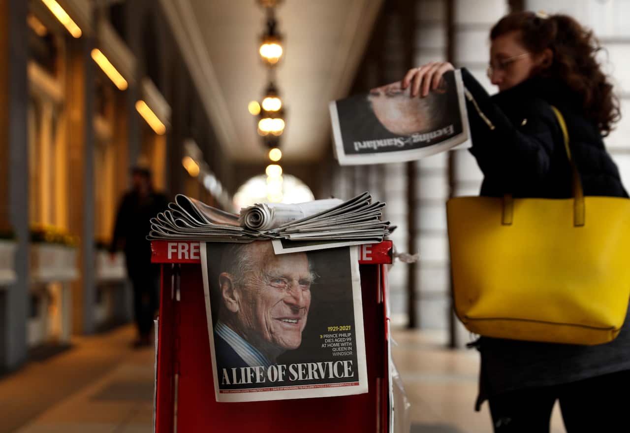 A woman picks up a newspaper with a tribute to Prince Philip on the front page at Leicester Square in London, Friday, 9 April, 2021.