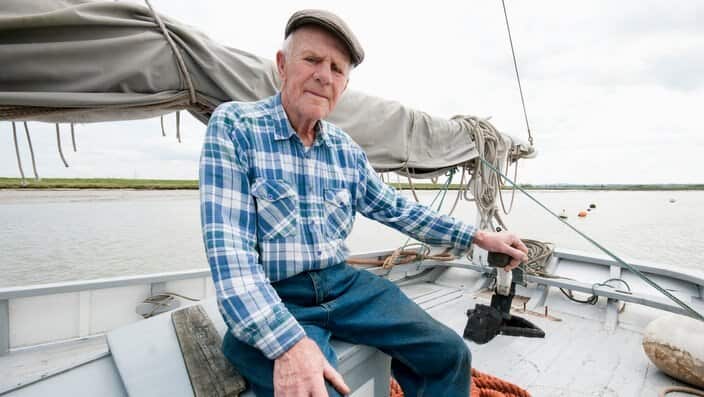 Fisherman sits on deck of boat with mast and sail