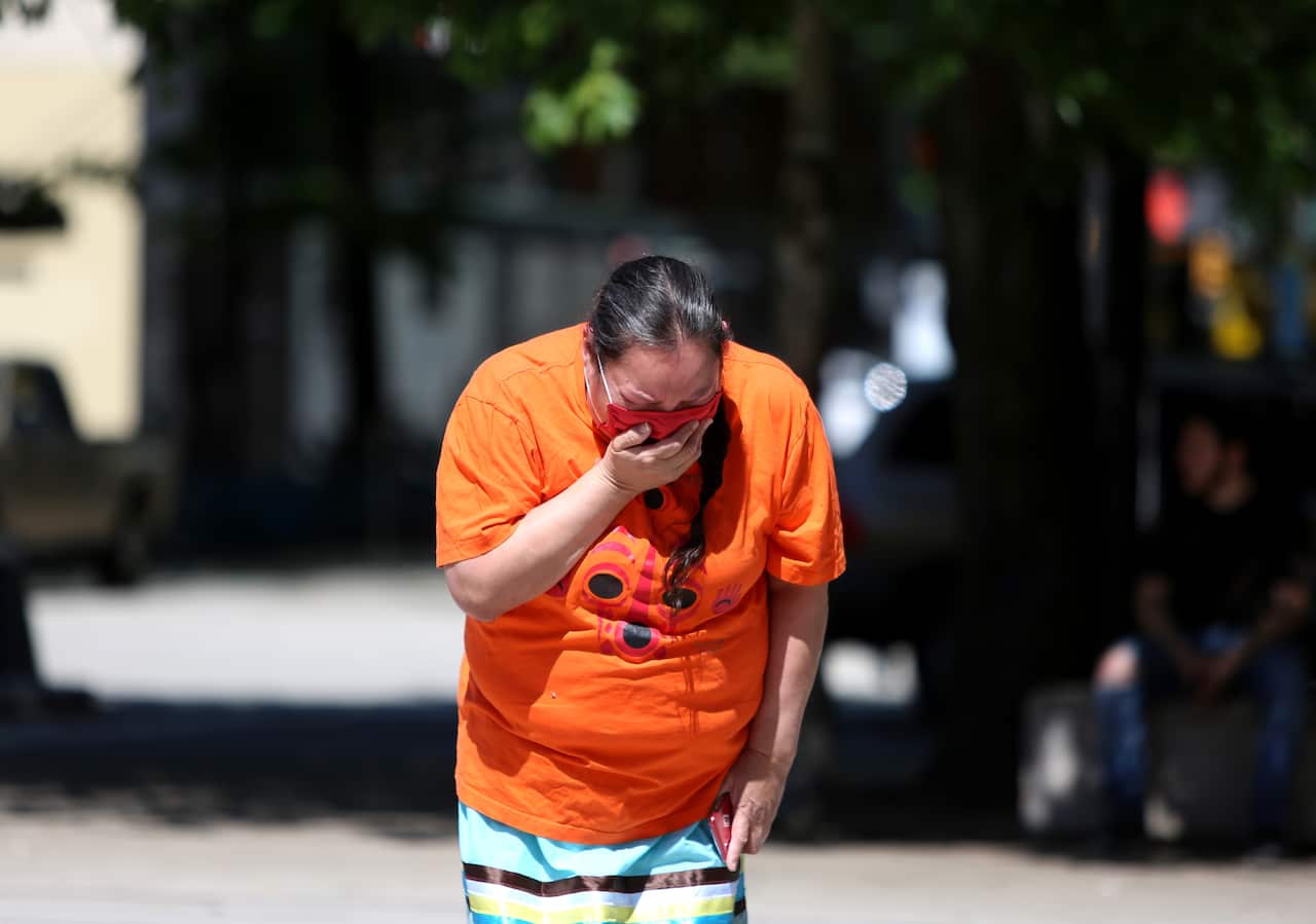 A woman mourns over 215 pairs of kids shoes outside Vancouver Art Gallery during a memorial on 29 May, 2021 in Vancouver, British Columbia, Canada.