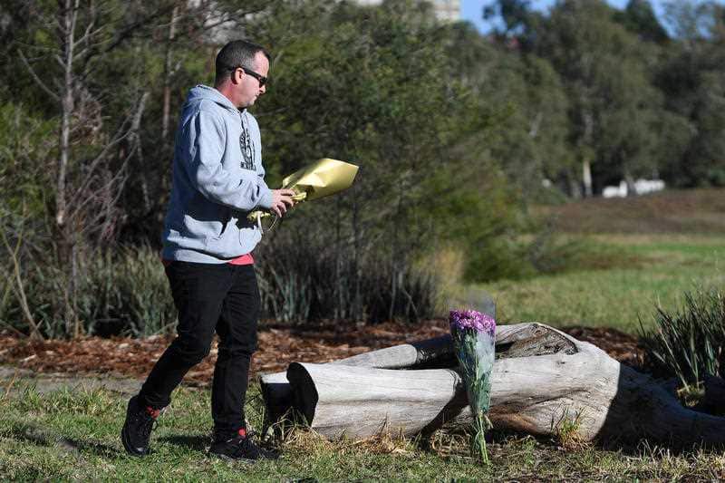 A man arrives to lay a bouquet of flowers at the site where Courtney Herron's body was found in Royal Park, Melbourne.