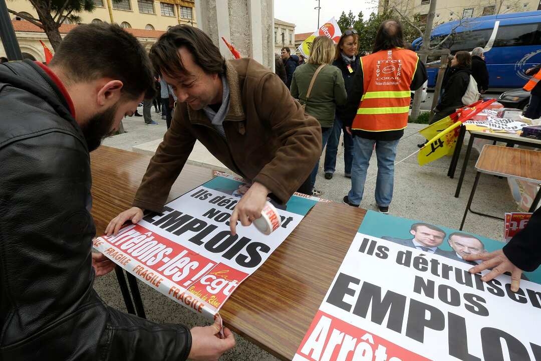 Rail workers stick posters reading "They kill our jobs, let's stop them".