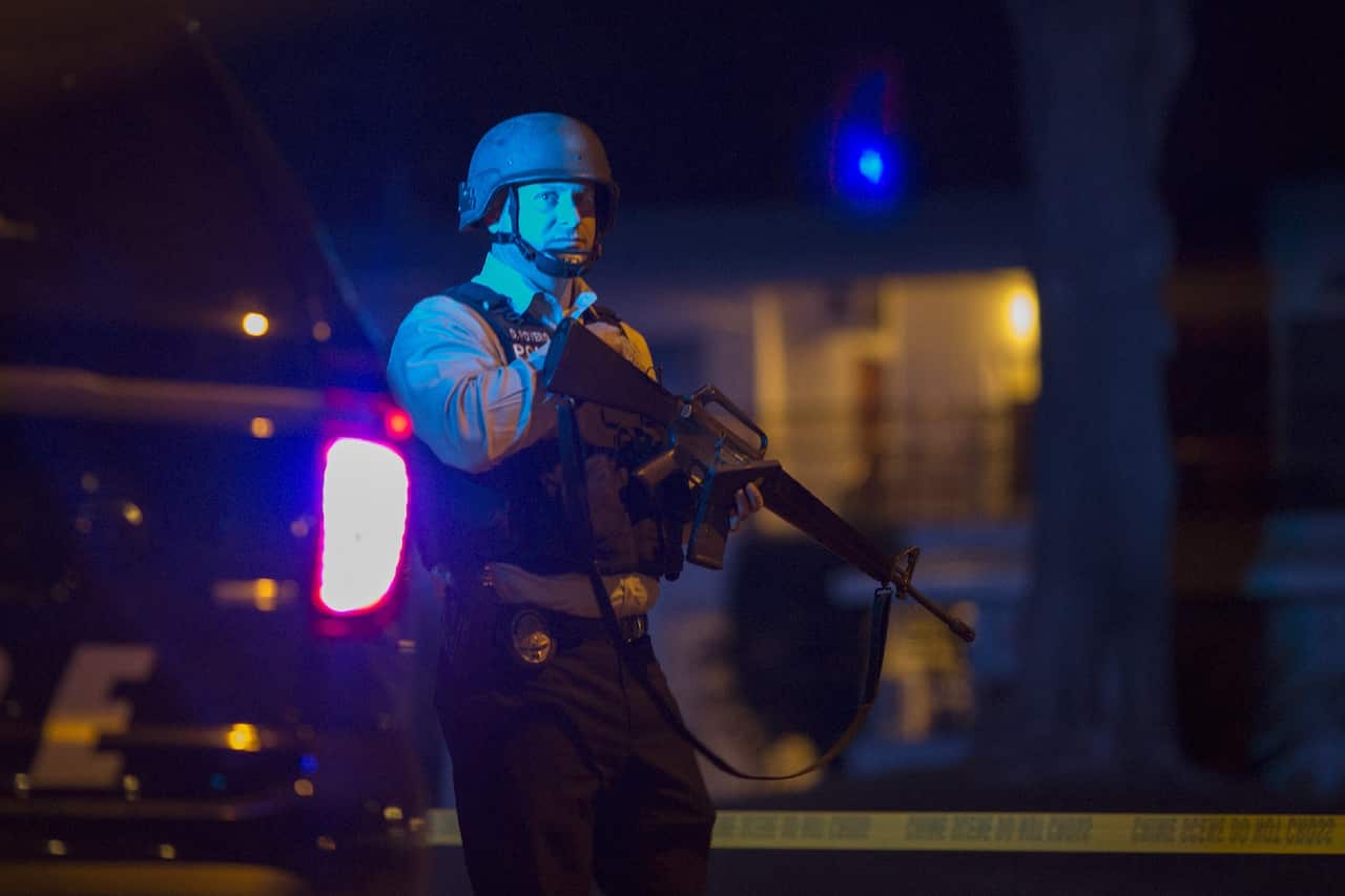 A police officer officer guards a police line as officers prepare to raid the home of one or more suspects of a mass shooting at the Inland Regional Centre by multiple gunmen.