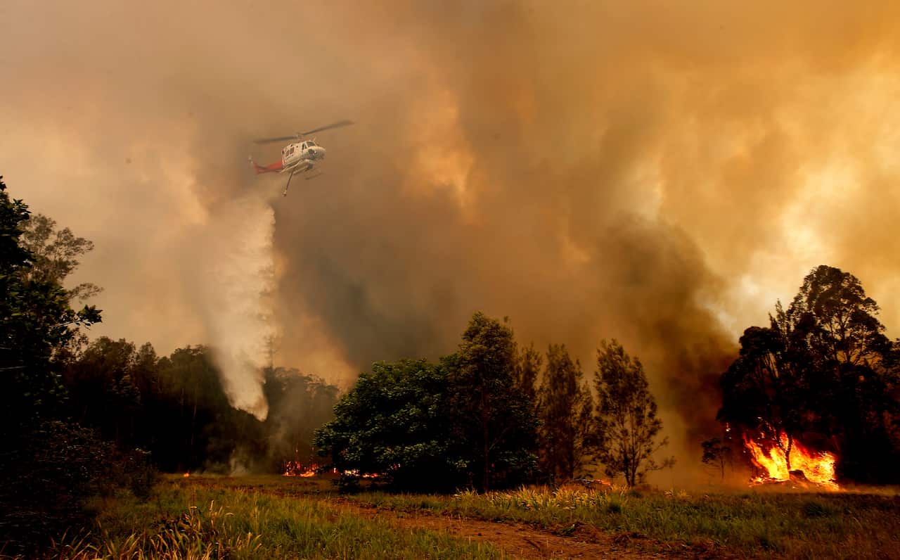 A fire bombing helicopter works to contain a bushfire along Old Bar road in Old Bar, NSW, 
