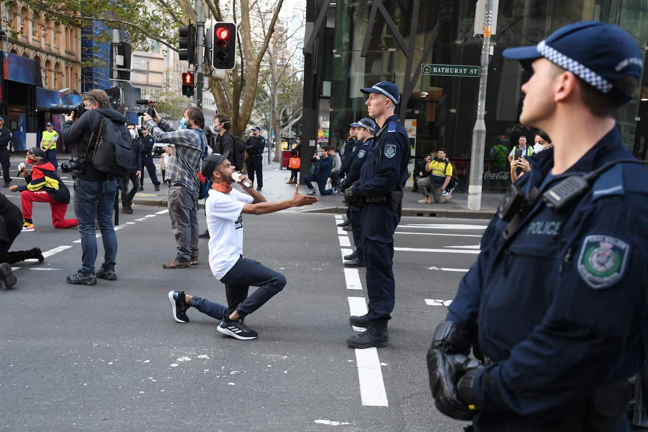 Man kneels and offers hand to officer in Sydney at the Black Lives Matter protest.