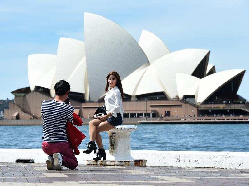 A man takes a photograph of a woman front of the Sydney Opera House