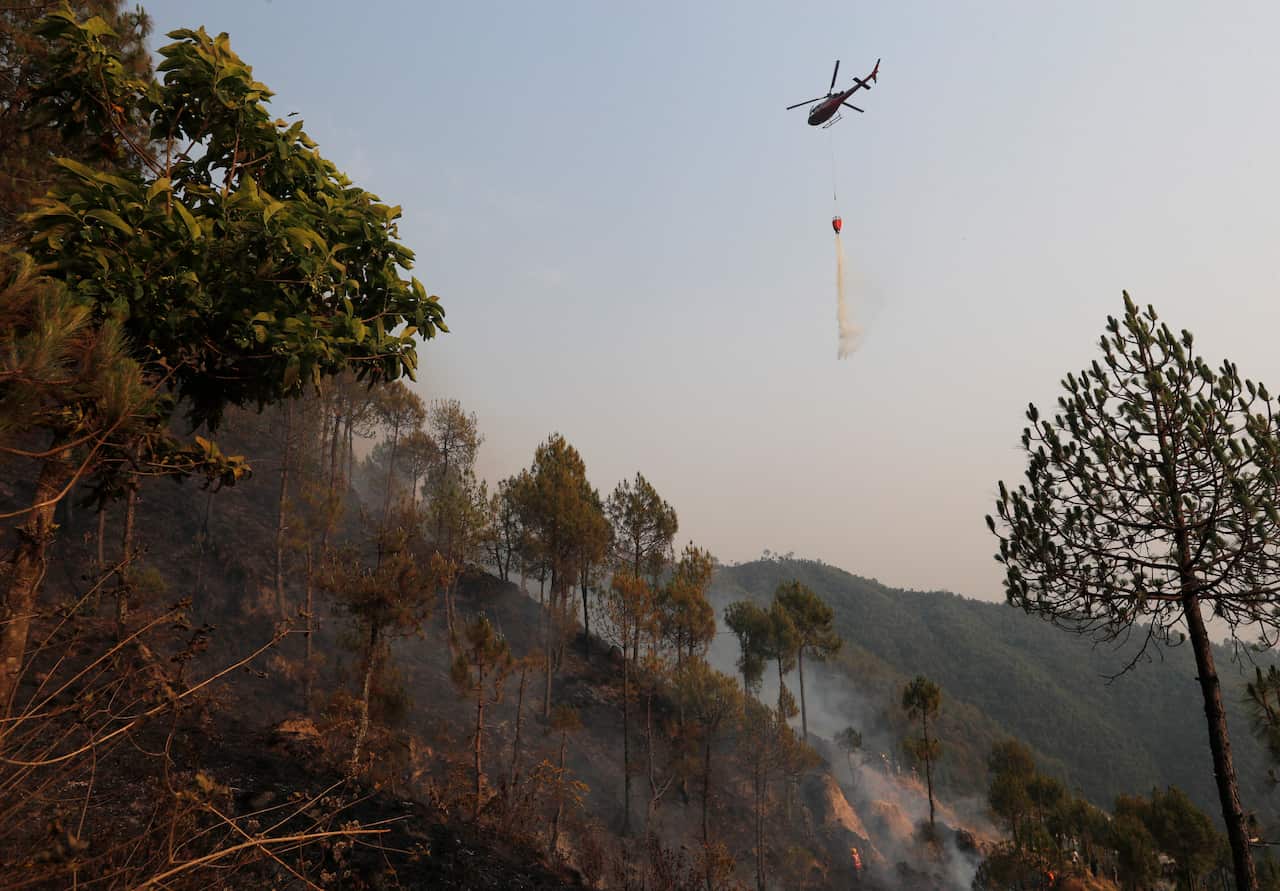 A helicopter pours water in an effort to douse a forest fire in Shivapuri National Park on the outskirts of Kathmandu, Nepal, Sunday, April 11, 2021. (AP Photo/Niranjan Shrestha)