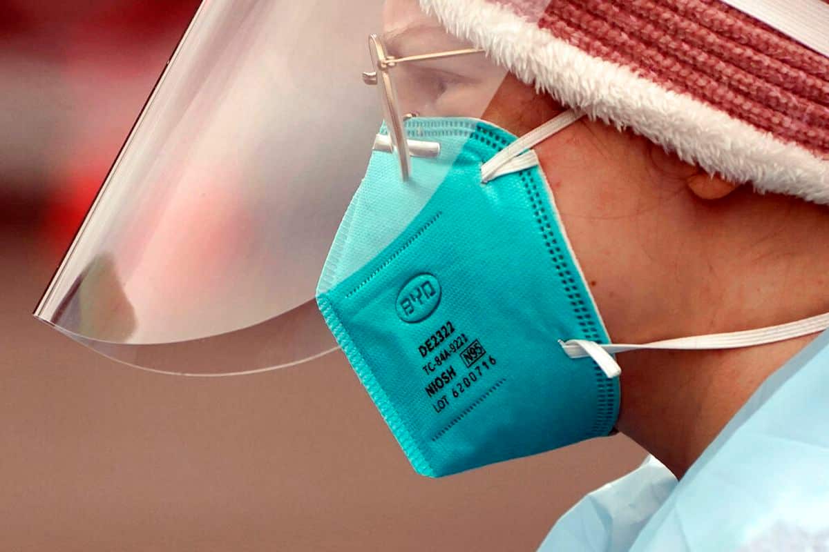 A medical assistant working at a drive-up COVID-19 testing clinic, wears an N95 mask